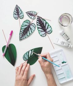 someone is painting leaves with watercolors on a white surface next to paintbrushes