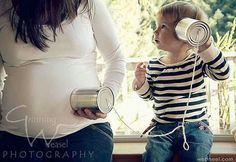 a pregnant woman holding a hair dryer to her head while standing next to a child