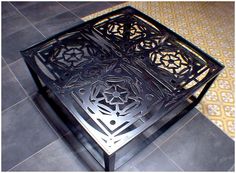 an intricately designed metal table sits on the floor in front of a tiled floor