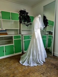 a white wedding dress is on display in a room with green cabinets and shelving