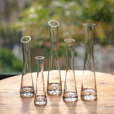 four glass vases sitting on top of a wooden table next to eachother