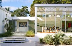 a white house with large windows and plants in the front yard