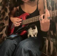 a woman sitting in a chair with a cat on her lap while playing an electric guitar