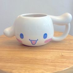 a white cup with blue eyes and pink ears on top of a wooden table next to a wall