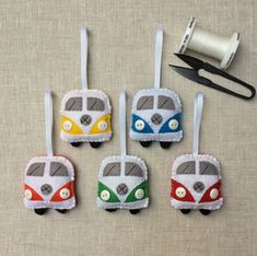 four felt bus ornaments are hanging on the wall next to scissors and thread spools