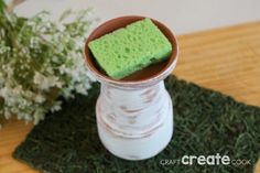 a vase with some green sponges in it sitting on a mat next to flowers