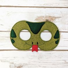 a green mask with a red bow hanging from it's side on a white wooden surface