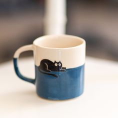 a black cat sitting on top of a blue and white coffee cup