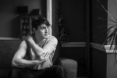 black and white photograph of a man sitting on a couch with his arms folded in front of him