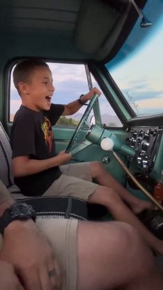 a young boy sitting in the driver's seat of a truck