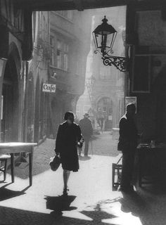 a black and white photo of people walking down the street in an old fashioned town