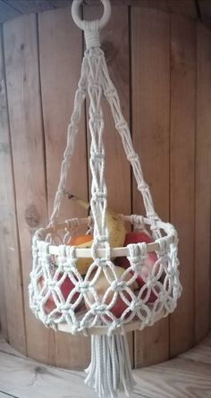 a white macrame hanging basket filled with apples and cheese on top of a wooden table