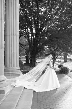 a woman in a wedding dress and veil is standing on the steps near some trees