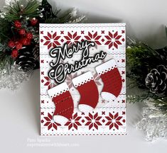 a christmas card with stockings and snowflakes on the table next to pine cones