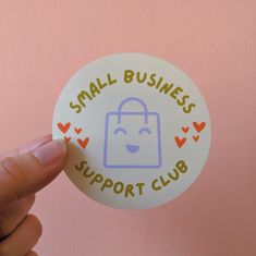 someone holding up a small round sticker that says small business support club