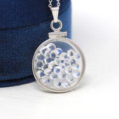 "Magical handcrafted brand new sterling silver genuine moonstone shaker locket! This whimsical pendant is dime sized with coin style bezels, and clear lucite covers. The round charm hangs from a brand new sterling silver chain, and is filled with approximately 2.5 carats of cabochon and round cut moonstone gems. An otherworldly piece of brand new gemstone jewelry, that features the optical phenomenon; adularescence! ERA - New METAL / MATERIAL - Sterling silver locket, sterling silver chain, luci Artisan Silver Jewelry With Moon Phase, Silver Moon-shaped Locket Jewelry, Silver Moon-shaped Jewelry With Coin Pendant, Silver Moon Phase Medallion Jewelry, Moonstone Pendant Amulet Jewelry, Moonstone Round Pendant Jewelry For Gift, Moonstone Amulet Pendant Jewelry, Silver Moon Phase Amulet Jewelry, Moonstone Amulet Jewelry Gift