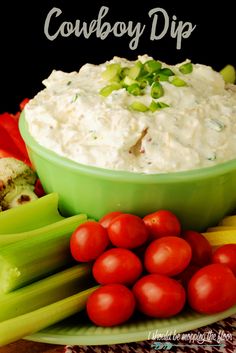 a green bowl filled with dip surrounded by celery and tomatoes