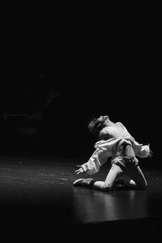 a man is sitting on the floor in front of a black background with his arms stretched out