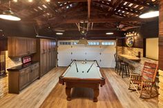 a pool table in the middle of a room with wooden floors and ceiling lights hanging from the rafters