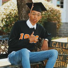 a man sitting on top of a bench wearing a graduation cap and holding a thumb up