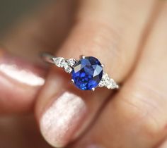 a woman's hand holding a ring with a blue sapphire and diamonds on it