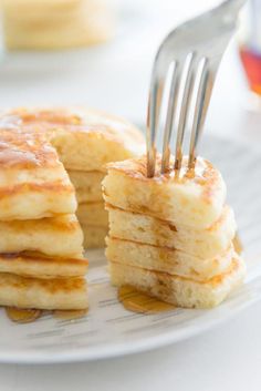 a stack of pancakes on a plate with a fork stuck in the top and syrup being poured over them