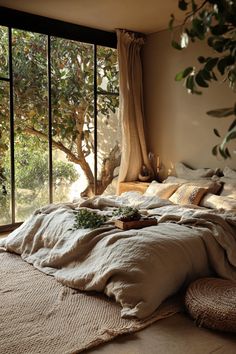 an unmade bed sitting in front of a large window next to a potted plant