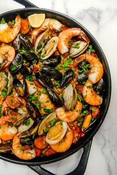 a skillet filled with seafood and mussels on top of a marble counter