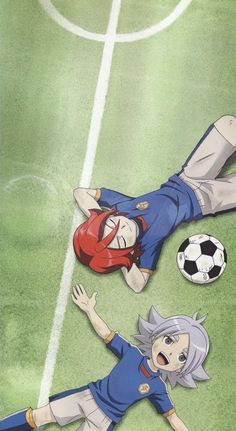 two people laying on top of a field next to a soccer ball in the air