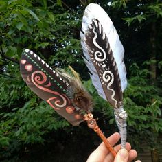 two feathers with designs on them being held by someone