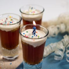 three glasses filled with liquid and topped with a birthday candle on top of a table