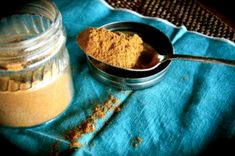 a spoon full of powder next to a jar on a blue cloth with a wooden spoon in it