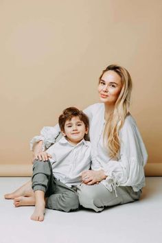 a mother and son sitting on the floor in front of a beige wall smiling at the camera