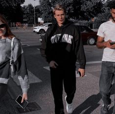 three people walking across a parking lot while looking at their cell phones