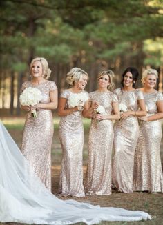 a group of women standing next to each other in front of trees and grass wearing dresses with sequins on them