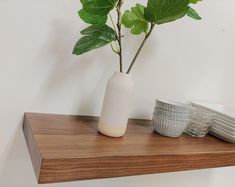 a white vase sitting on top of a wooden shelf filled with plates and cups next to a green leafy plant