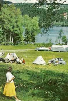 a group of people camping in a field next to a lake with cars parked on the grass