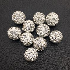 several silver colored round beads on a black leather surface with white and clear crystals in the middle