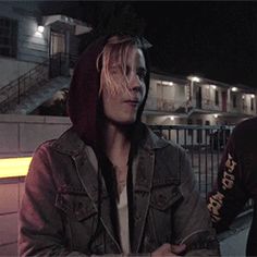 two young men standing next to each other in front of a building at night with lights on