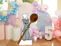 a cartoon mouse holding a wooden sticker in front of balloons and decorations for a birthday party