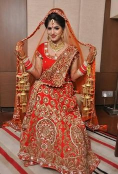 a woman in a red and gold bridal gown sitting on a chair with her hands up