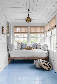 a room with blue floors and white walls, including a bed in the corner between two windows