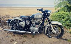 a motorcycle parked on the side of a dirt road next to some bushes and trees