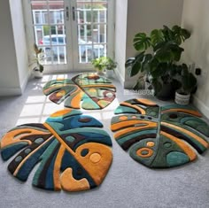 four colorful rugs on the floor in front of a window with potted plants