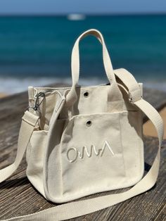 an omu bag sitting on top of a wooden table next to the ocean and blue sky