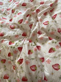 an unmade bed with strawberrys and flowers on the comforter, next to a pillow