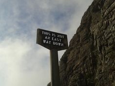 this is not an easy way down sign on the side of a mountain with clouds in the background