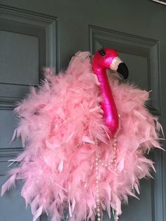 a pink flamingo wreath hanging on the front door with beads and pearls around it