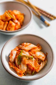 two white bowls filled with food next to chopsticks