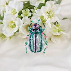 a green and pink beaded beetle sitting on top of white flowers in front of it